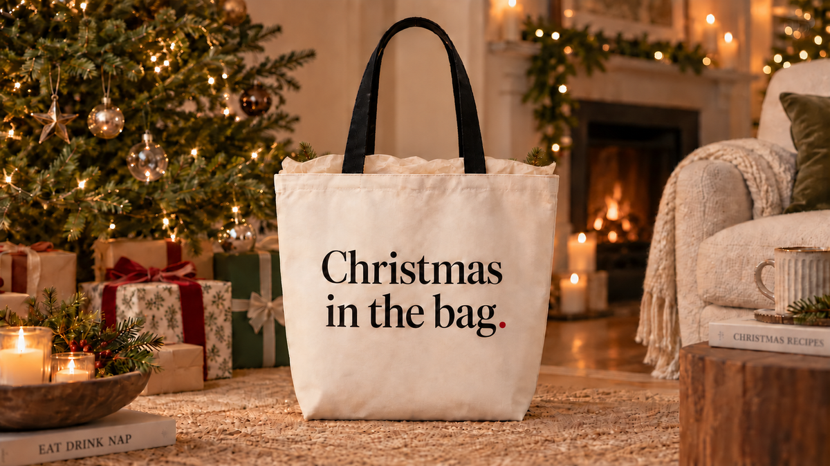 Christmas in the bag tote beside a Christmas tree and fireplace